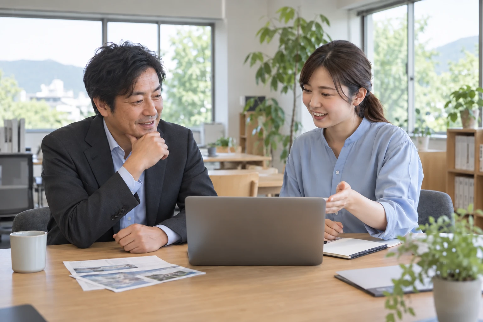 明るいオフィスで、右側の担当者が左側の法人のお客様にパソコンを使って説明するイメージ